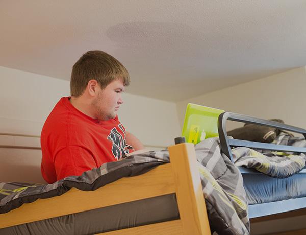 Male student laying on a lofted bed with his laptop.
