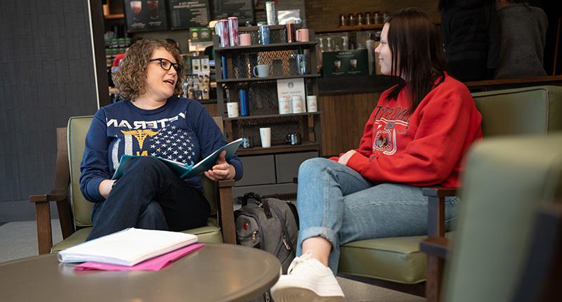 Two females in comfortable chairs, chatting in a coffee shop.